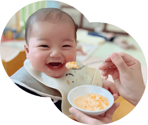 ピンクのエプロンをつけて給食を食べる園児